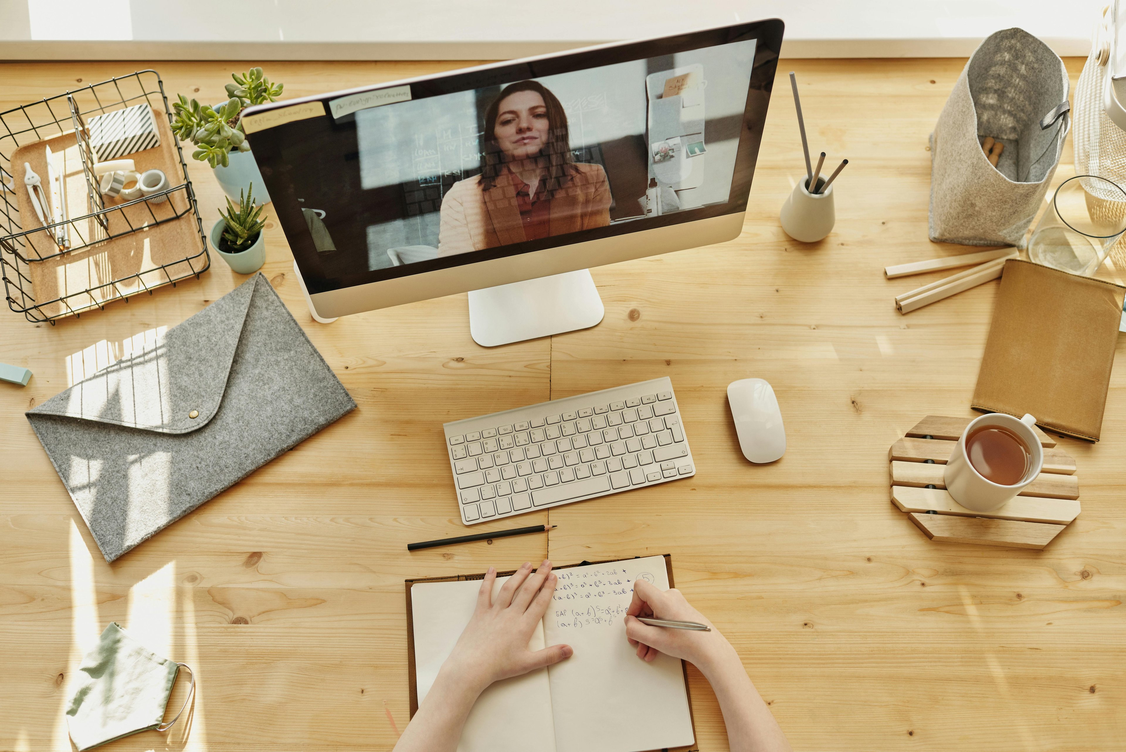 wom speaking on a monitor screen, person sitting in front of it taking notes