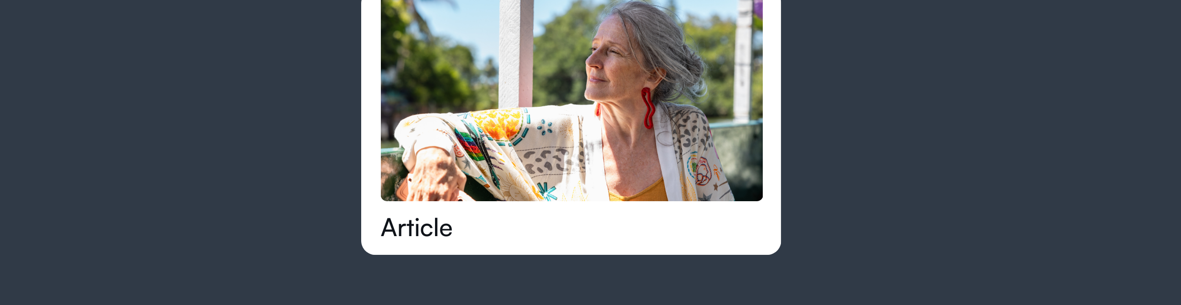 "An elderly woman with gray hair sitting outdoors, looking thoughtful and content, wearing a colorful patterned shawl, with a sunny, green background."