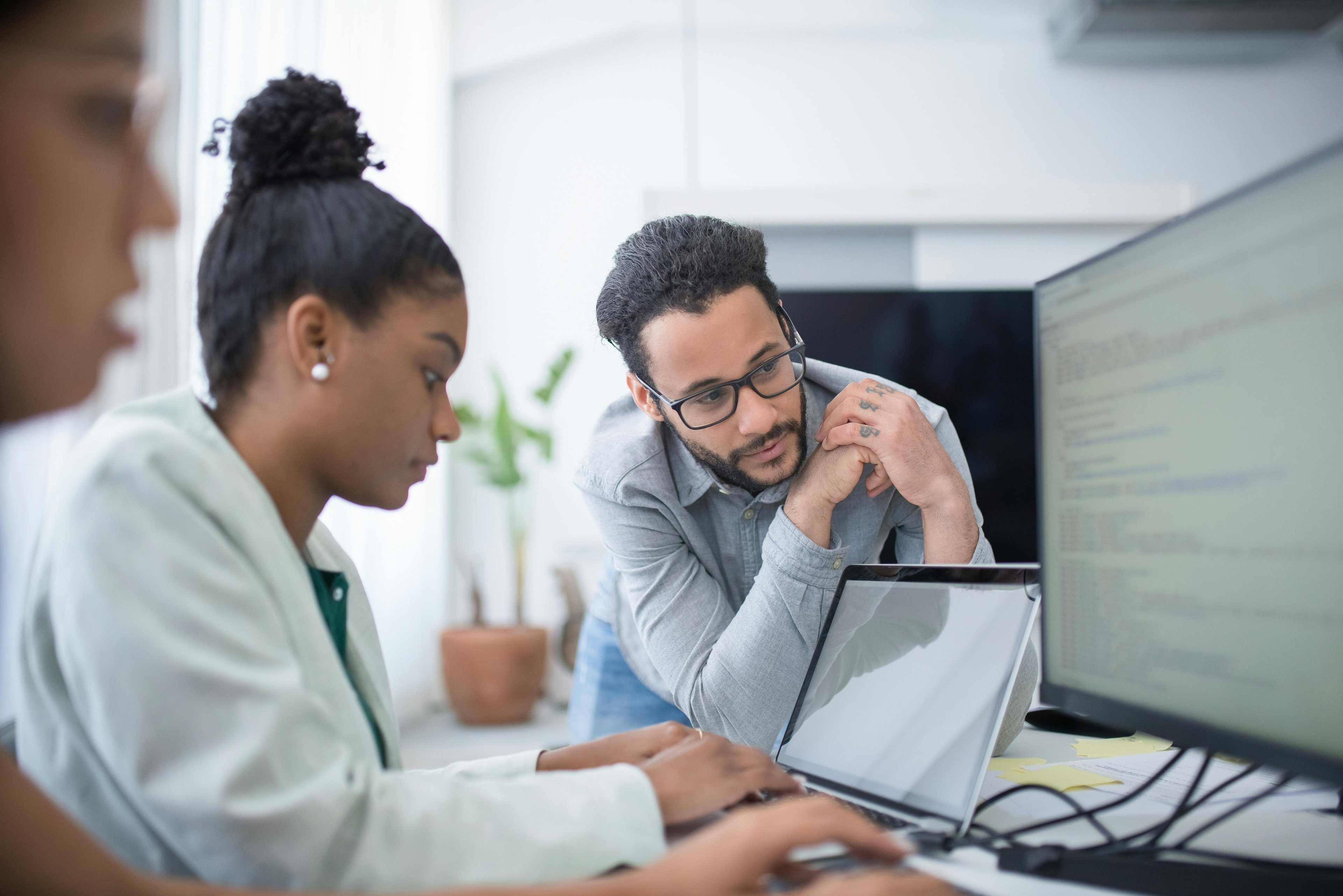 woman working on laptop, man next to her gives support